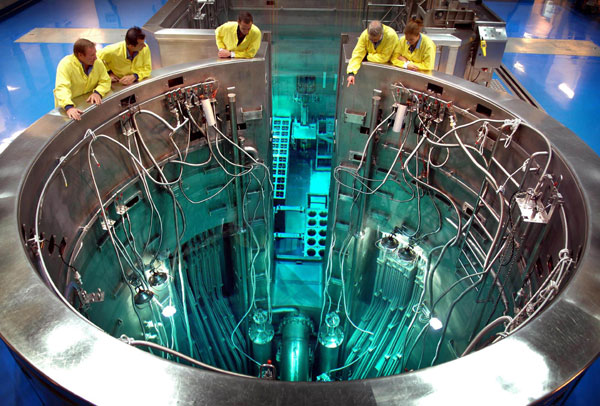 ANSTO's OPAL Reactor from above, with four staff members inspecting it in yellow coats.