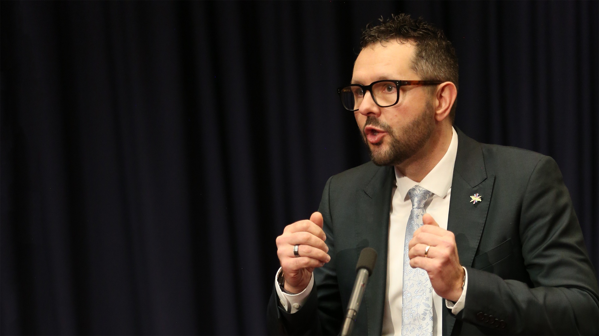 Professor Mark Hutchinson wearing a suit and tie and dark -rimmed glasses speaking at a lecture. Hope Oration.
