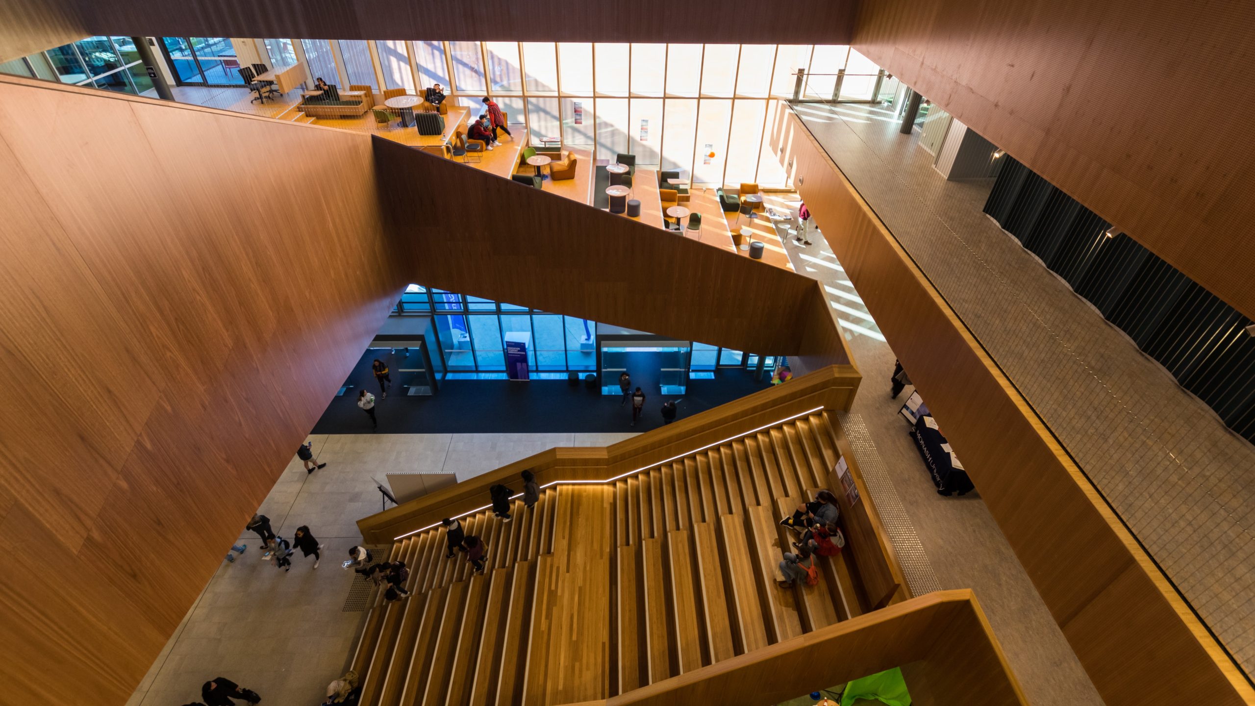 Photograph of an open artrium at a university looking down on wooden stairs that double as lecture seating.