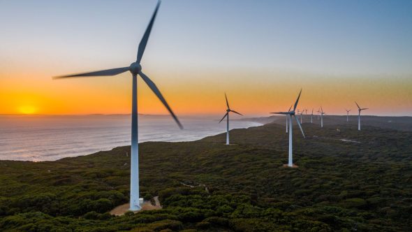 Wind turbines embedded in vegetation along the coastline. The sunsets of the coast of Australia in the background.