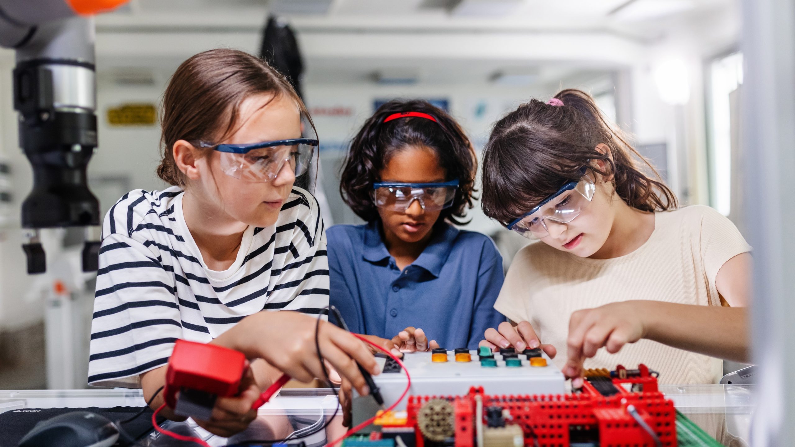 three girls wearing safety glasses working on a circuit board