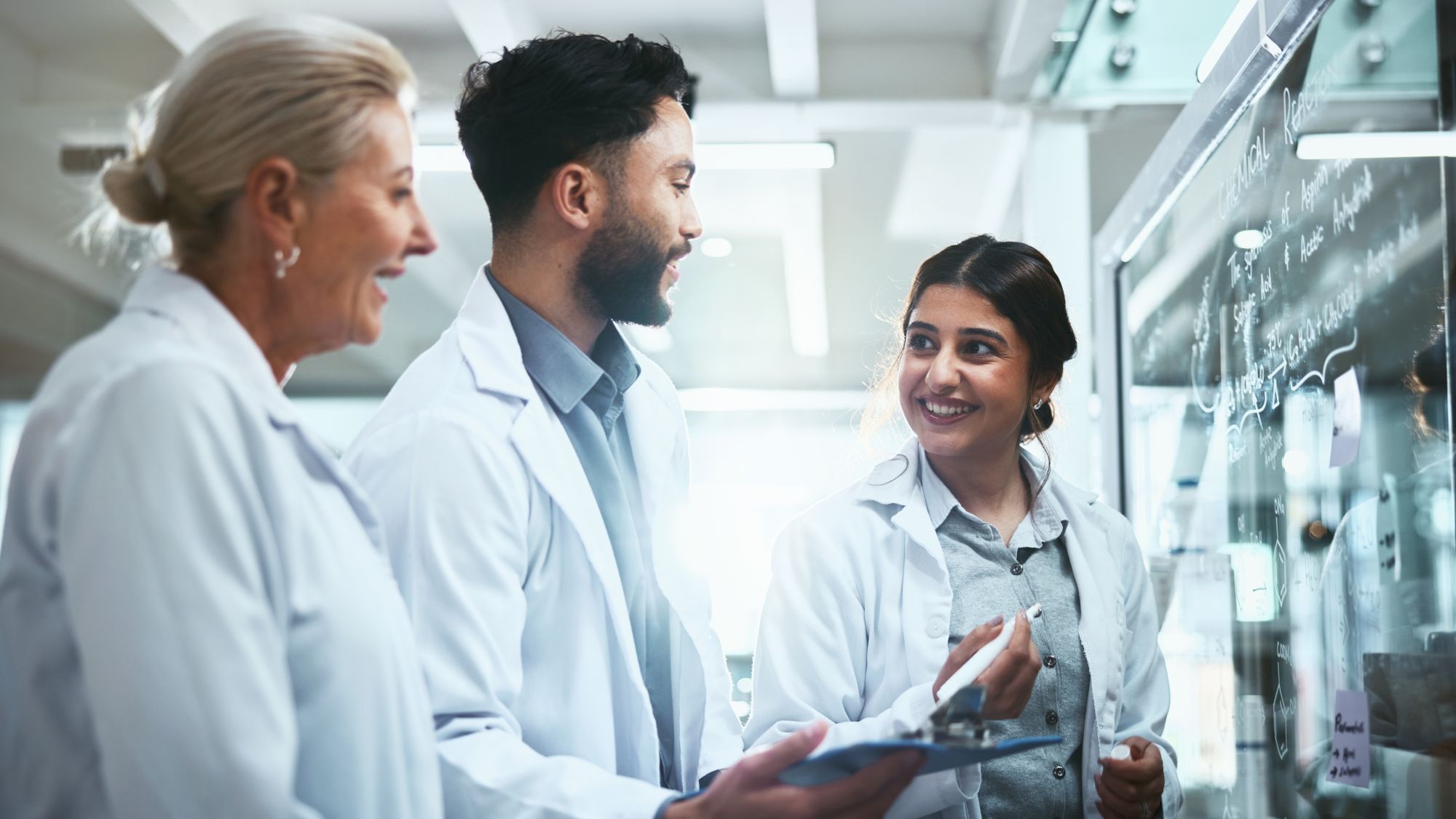 Three people wearing lab coats chatting in a lab.